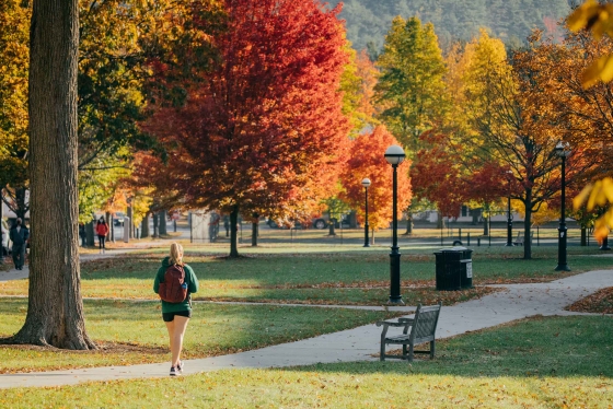 Student walking across campus with trees in full foliage