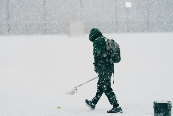 Lacrosse playing scooping balls up from the snowy practice field