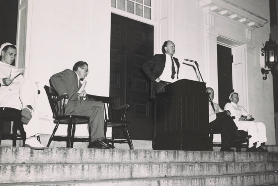 President John Sloan Dickey '29 speaks on the steps of Dartmouth Hall on Dartmouth Night, Oct. 1954. From left, sitting, are Sidney Hayward '26, secretary of the College, Coach Tuss McLaughry, and Lou Turner '55, captain of the football team.