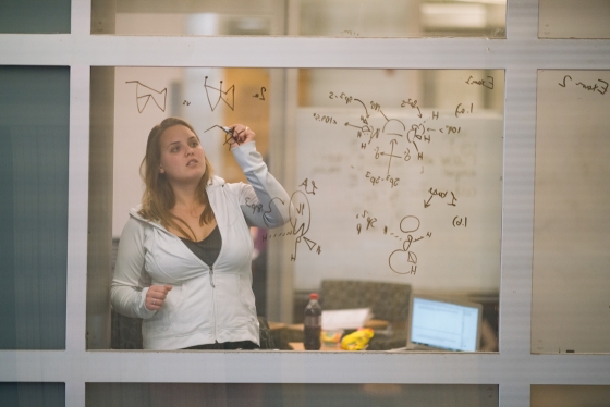 Student writing mathematical formulas on glass wall