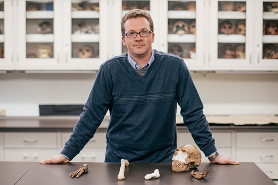 Jeremy DeSilva standing behind a table with 3D printed versions of the discovered homo naledi fossils