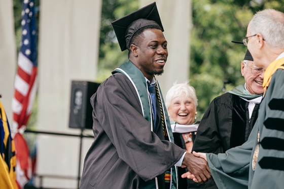 Theo Wilson in his graduation cap and gown shaking hands with President Phil Hanlon