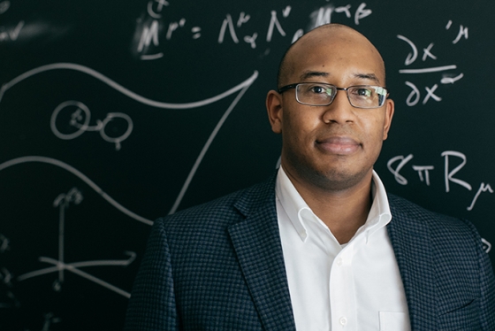 Devin Walker standing in front of a chalk board with scientific equations written on it