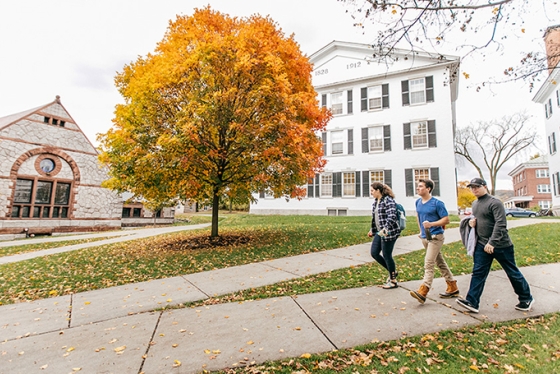 three students walking down the sidewalk near Rollins Chapel, a tree with yellow and orange leaves behind them