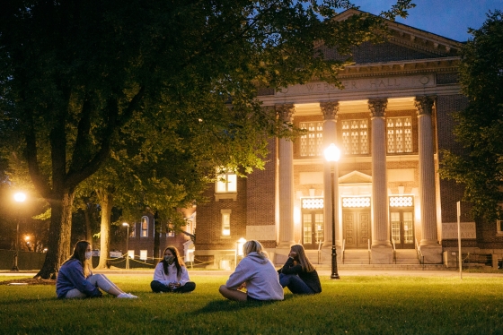Masked students sitting on the Green at dusk across from Rauner Library