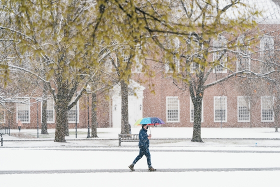 A man walking on the Green holding a colorful umbrella during a snowstorm
