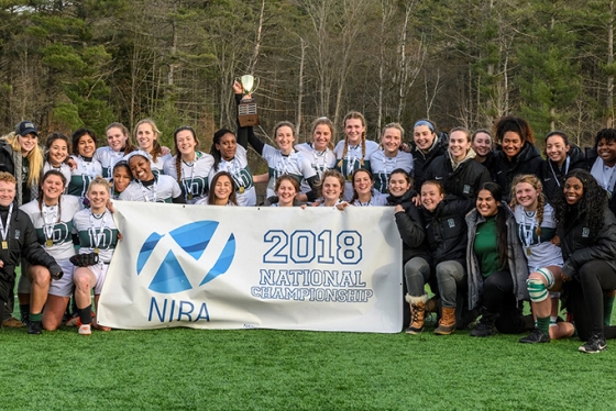 the women's rugby team posing with a white and blue banner that reads 2018 National Championship