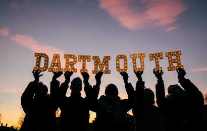 Silhouettes of students holding up letters that spell "Dartmouth" around sunset.