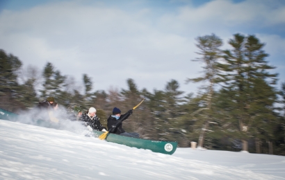 Students racing down a ski slope in a green canoe