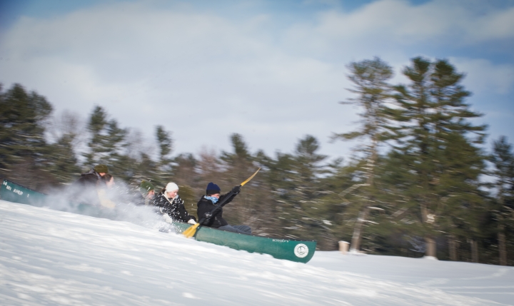 Students racing down a ski slope in a green canoe