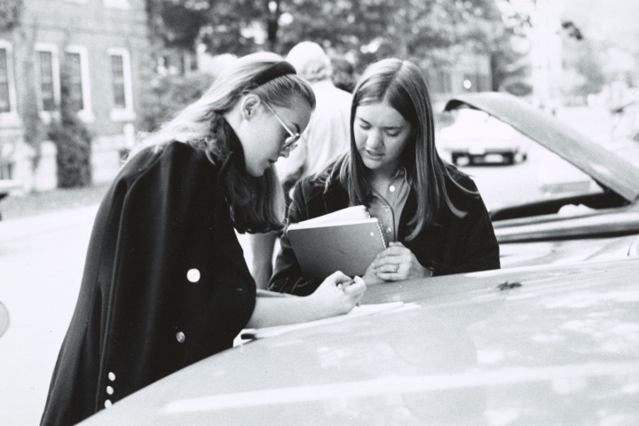Two women writing notes on top of a car hood