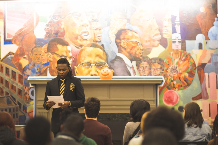 Rothschild Toussaint reading a poem in front of a mural of activists