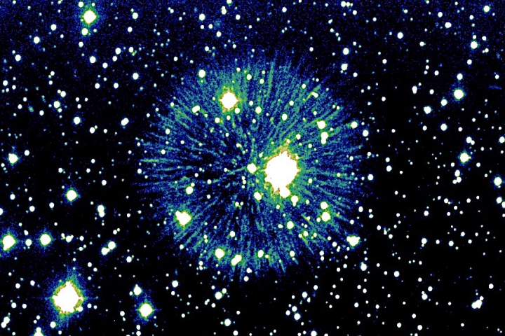 Blue, green and white burst of light centered on black background covered in stars