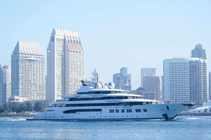 Large yacht traveling on water with city in the background.