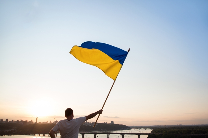Man waves Ukrainian flag near river in Kyiv.