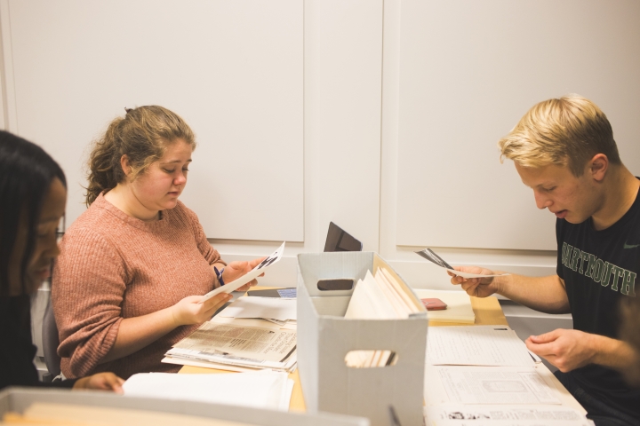 Three students seated around a table look through papers from the collection of Errol Hill.
