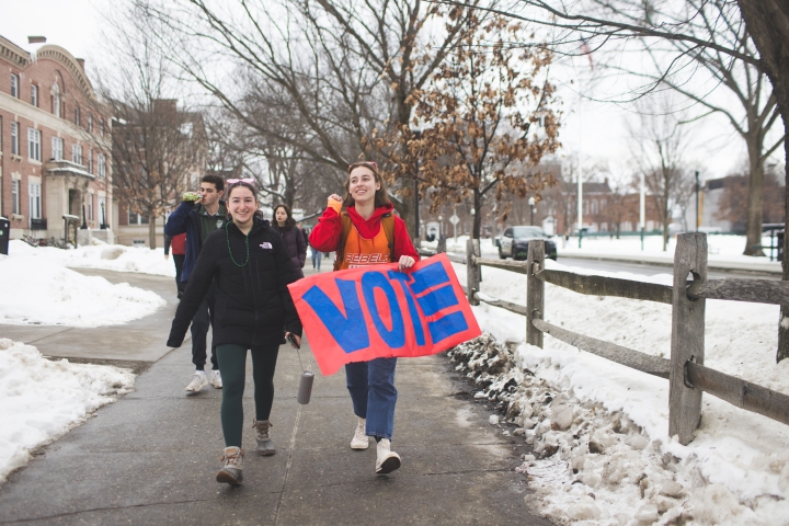 Two students holding a colorful VOTE sign lead students to vote.