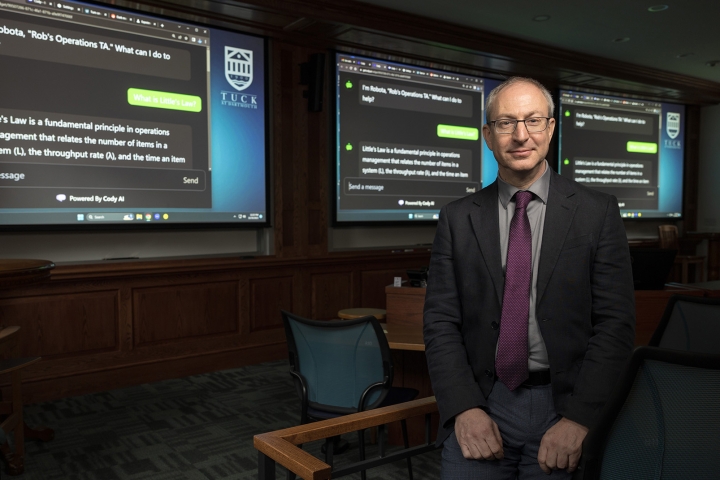 Tuck professor Rob Shumsky in front of large screens of terxt