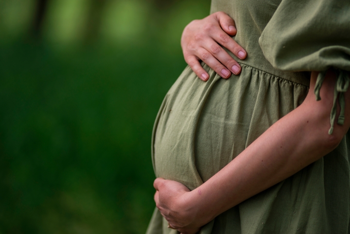 Pregnant woman in a summer green dress touches stomach