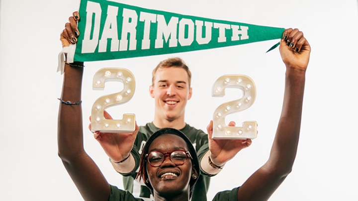 a female student holding a Dartmouth pennant above her head and a male student holding the number 22 behind her