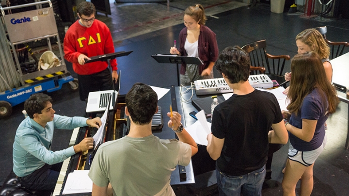 students gathered around a piano rehearsing a play