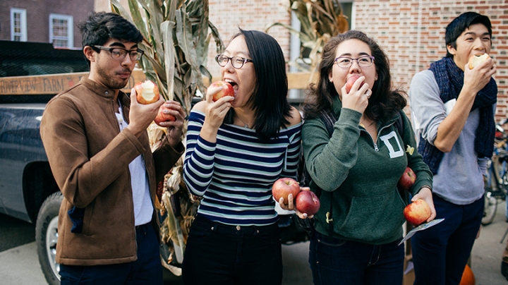 four students standing next to each other eating apples