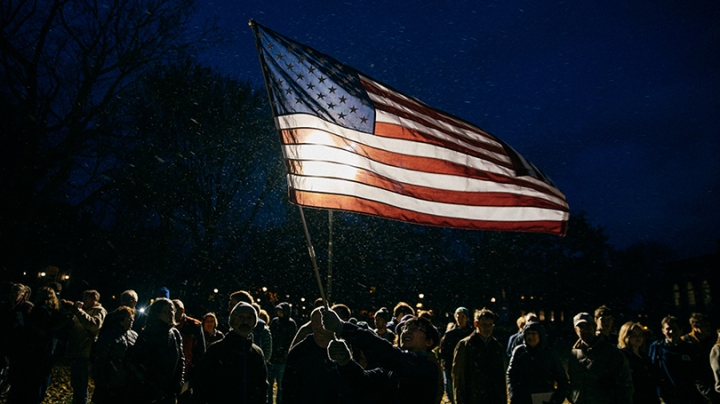 veterans gathered on the green at night waving an American flag