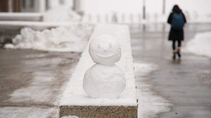 a miniature snowman sitting on a granite ledge