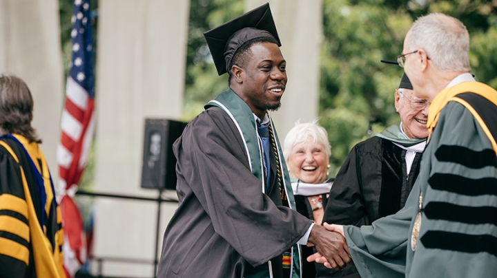 Theo Wilson in his graduation cap and gown shaking hands with President Phil Hanlon