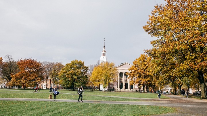 students walking across the Green with yellow foliage and Baker Tower in the background