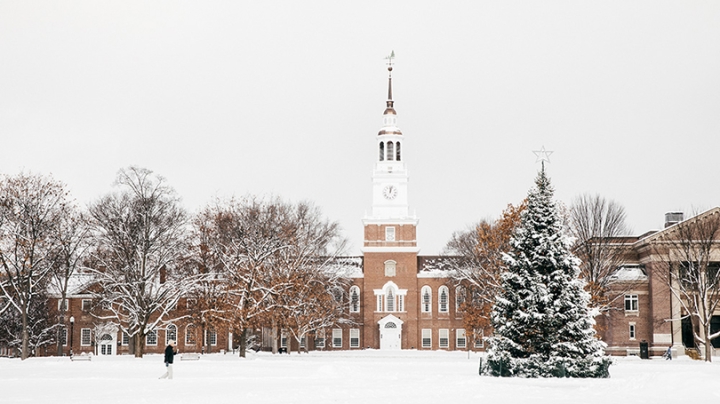 a person walking across the snow-covered Dartmouth Green in front of Baker-Berry Library