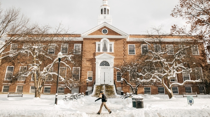 a person walking in front of Baker Library in the snow