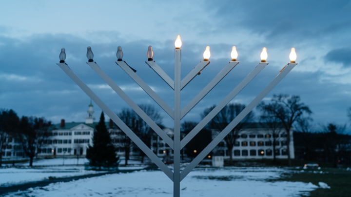A menorah with five lit up lights on the Green at dusk.