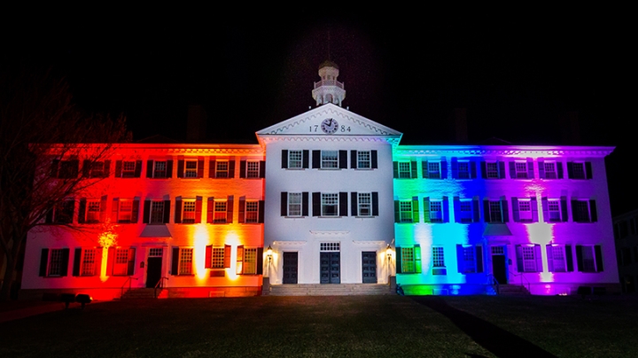 Dartmouth Hall lit up with red, orange, green, blue, and purple lights