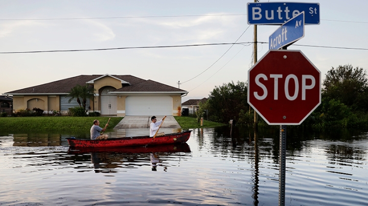 two people paddling a canoe up a flooded street in Florida