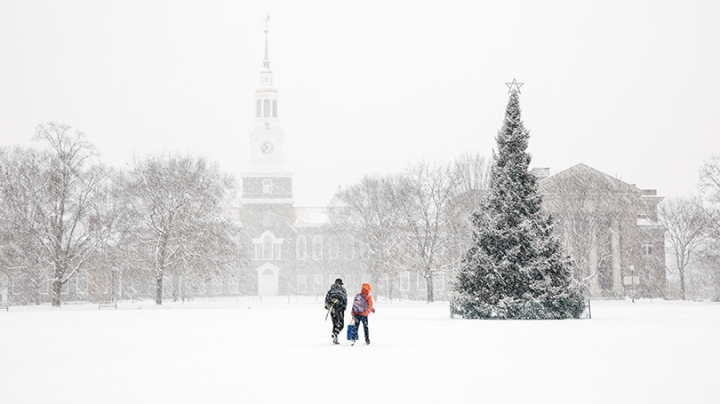 students crossing the snow-covered green with a Christmas tree in the background