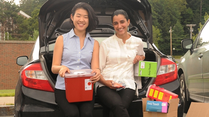 two girls holding boxes, standing in front of the trunk of a car