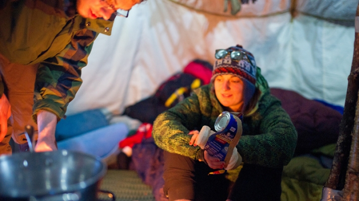 a student sitting by a fire with a can of biscuits in her hand