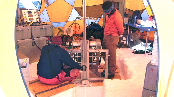 two men operating an ice drill under a tent