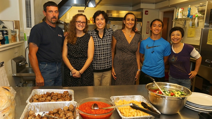 a group of Dartmouth staff members and friends standing together behind a spread of food they cooked