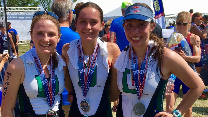 three female triathletes standing together and wearing their medals