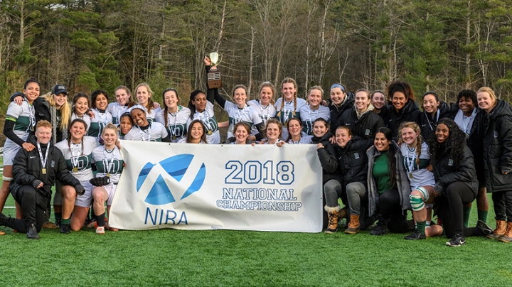the women's rugby team posing with a white and blue banner that reads 2018 National Championship 