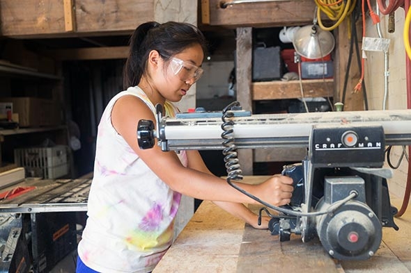 Katie Zhang ’16 cutting wood with a power saw