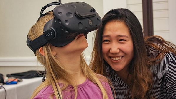 a woman watching another woman testing a virtual reality device