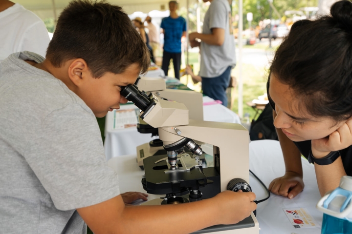An attendee peers into a microscope to view a slide while a graduate student from Dartmouth’s STEAM Outreach Program looks on. (Photo by Eli Burakian ’00)