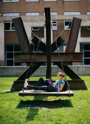 A students rests on a sculpture behind the Berry Library