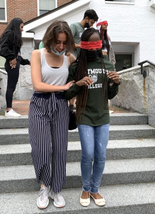 A blindfolded student being led down steps by another student.