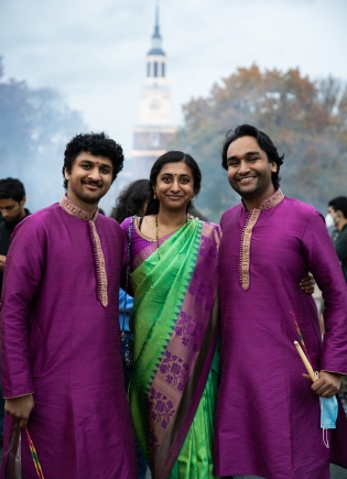 Three people in traditional Hindu dress in front of Baker Tower