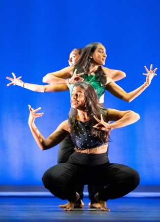 Members of dance troupe Raaz performing against a vivid blue background