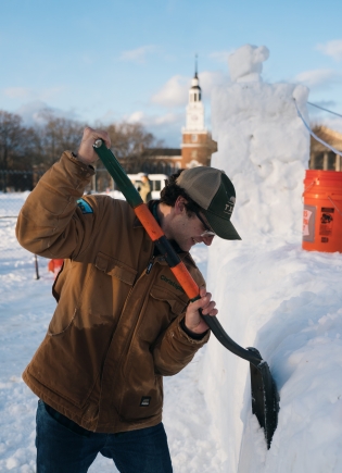 A person carving the snow sculpture with a shovel